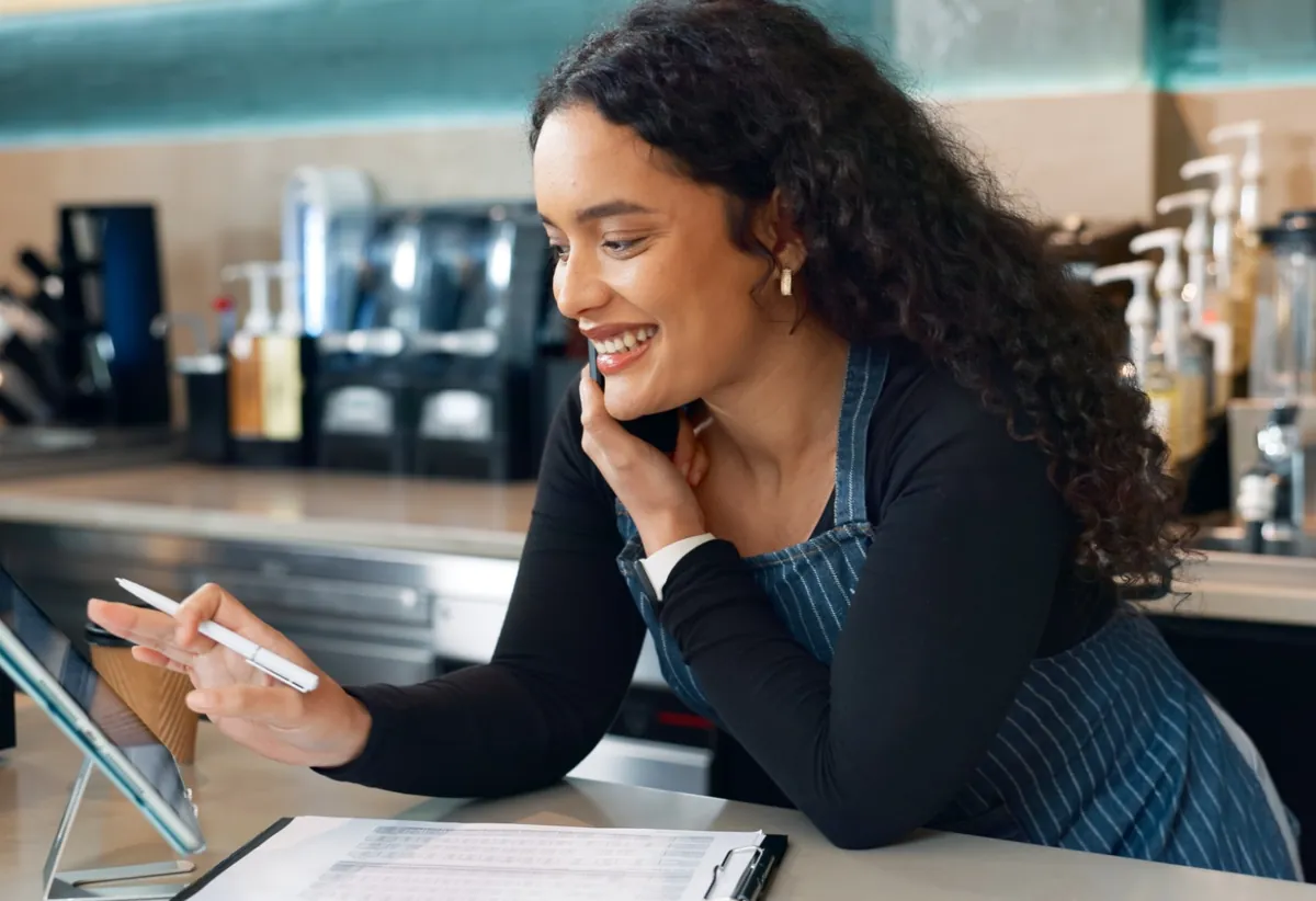 Dona de café sorrindo ao atender uma ligação no balcão